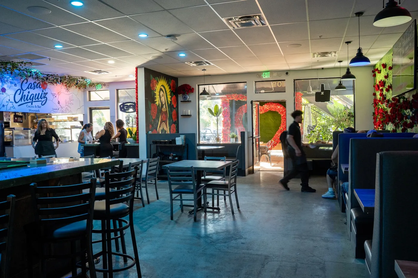Wide dining room view with blue booths, bar and Guadalupe mural toward the entrance
